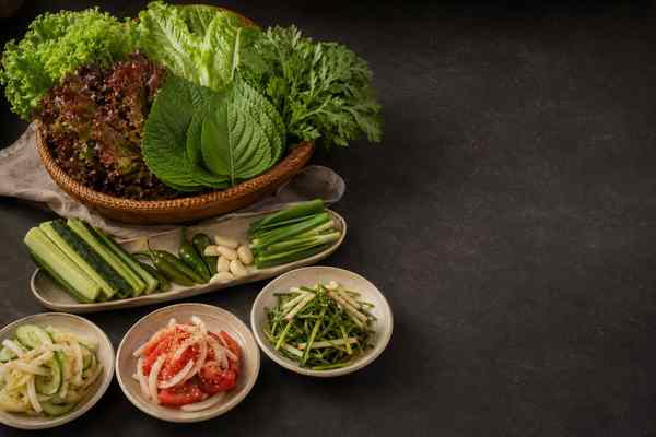 Basket of assorted lettuces, perilla, and crown daisy; a plate of cucumber sticks, green chilies, garlic, and scallions; three bowls of dressed salads.