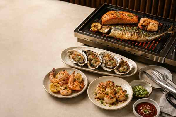 Grilled shrimp, fish, and shellfish arranged with clean serving dishes on a Korean barbecue table.