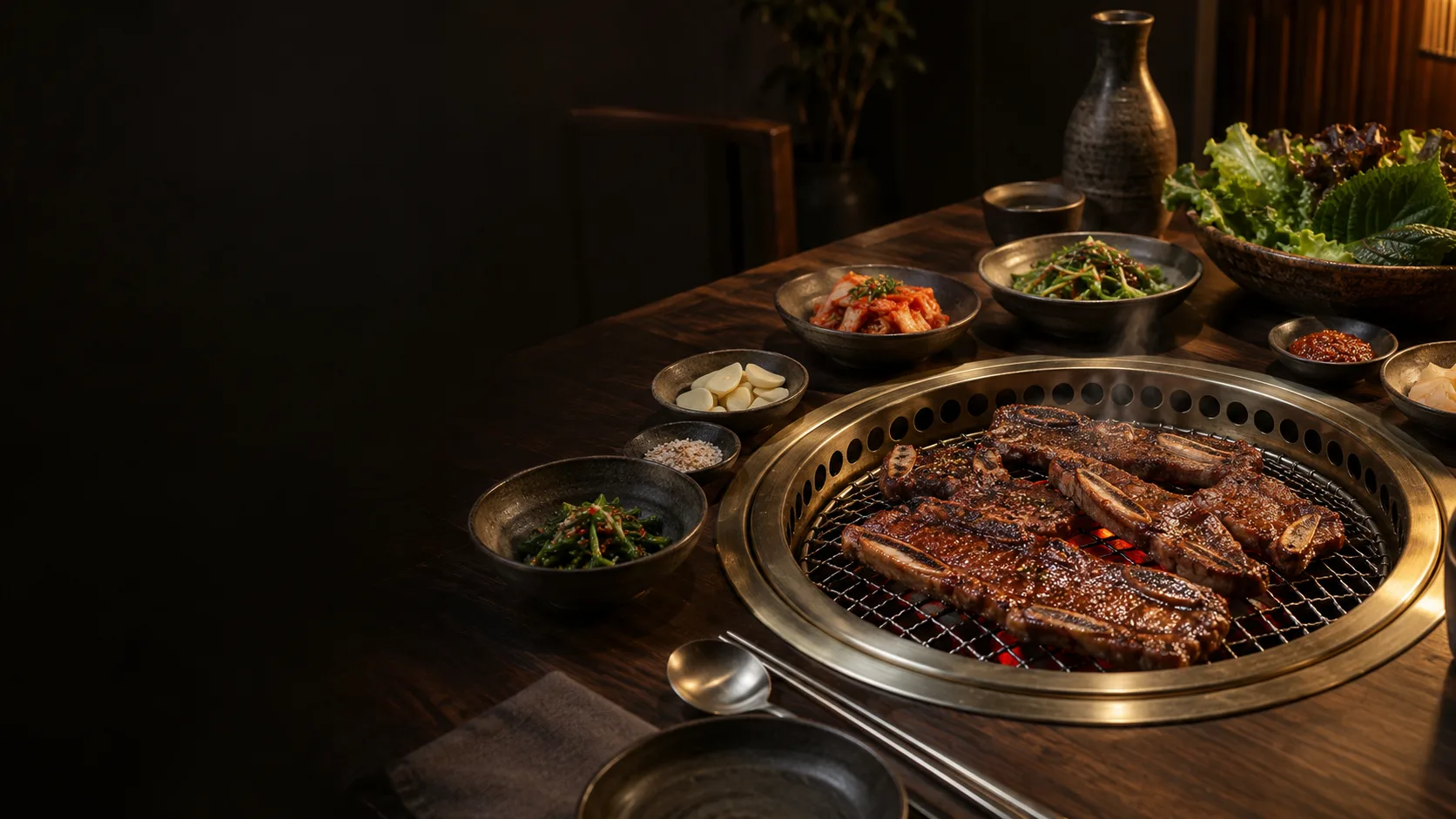 Korean beef short ribs on a glowing tabletop grill, surrounded by banchan and lettuce in warm evening light.