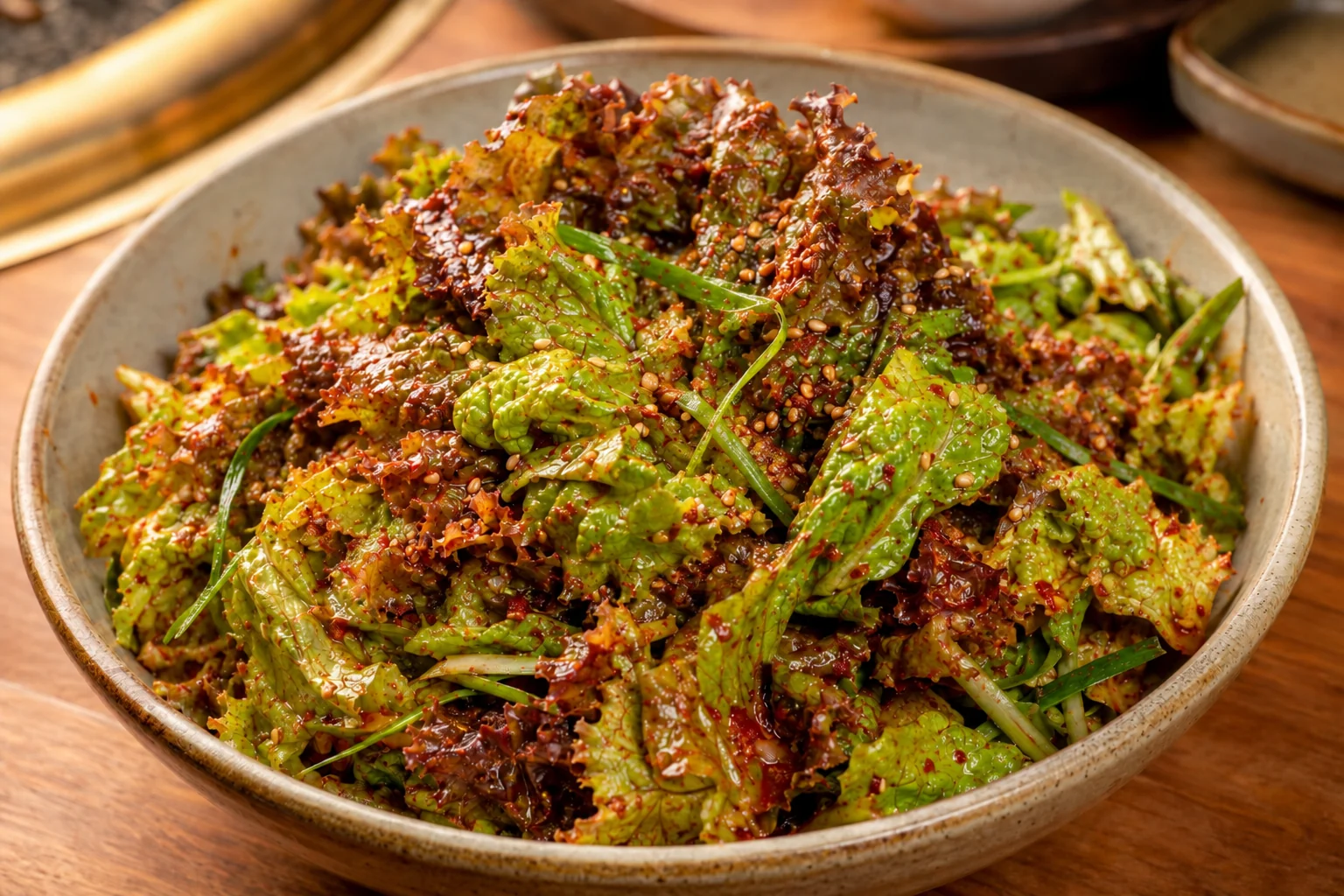 Green and red leaf lettuce with scallion, red chili dressing and sesame in a shallow ceramic bowl.